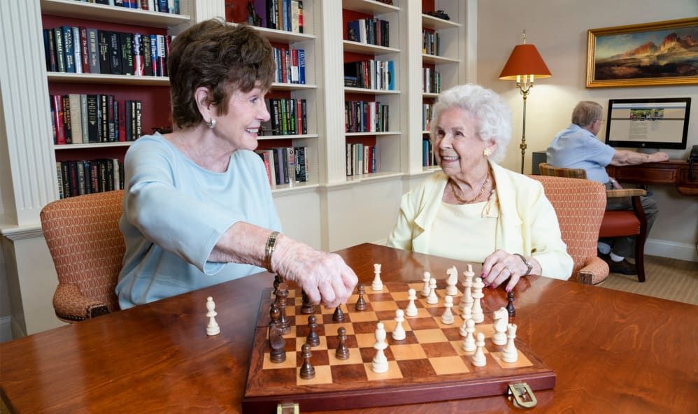 Two elderly women enjoying a game of chess in a library setting.