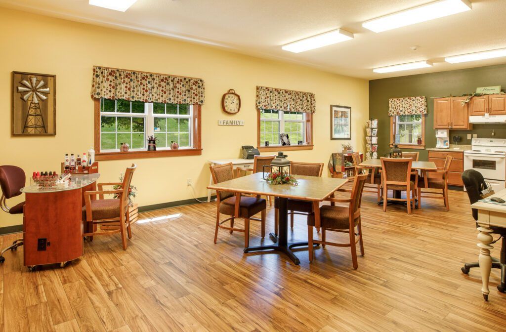 A cozy dining room with wooden flooring, featuring several tables and chairs, decorated with wall art and large windows.