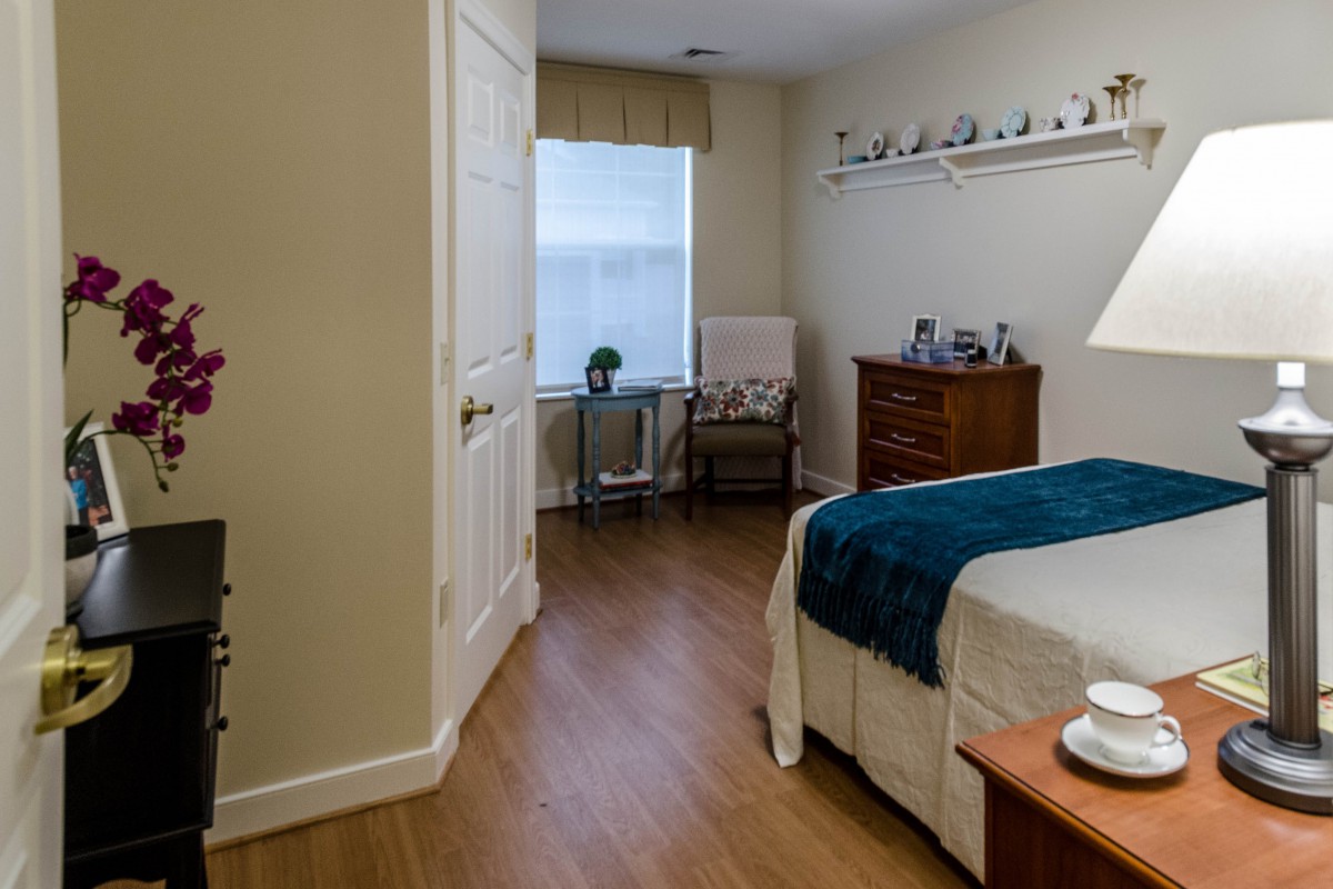 A cozy bedroom with a neatly made bed, dresser, and a chair by the window.