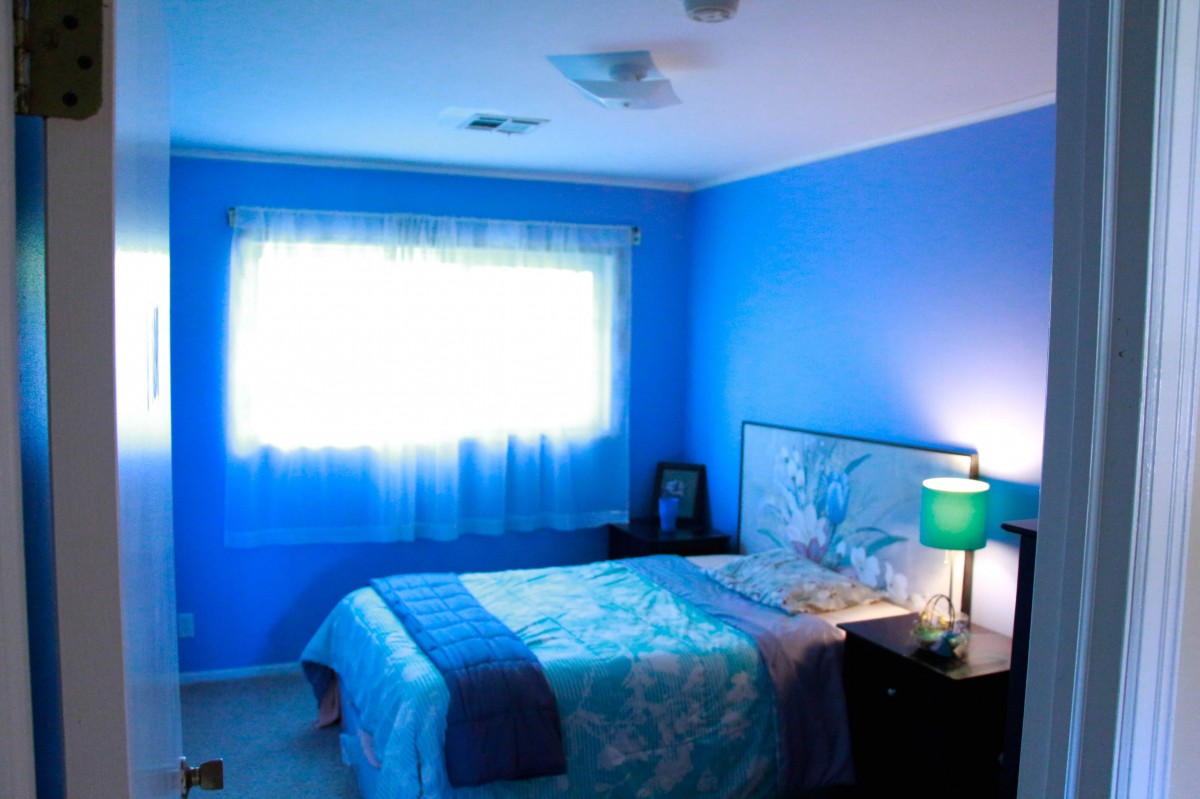 A cozy bedroom with bright blue walls and a softly lit lamp.