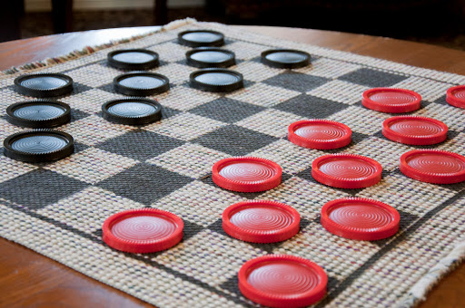 A checkers game in progress, featuring black and red pieces on a patterned board.