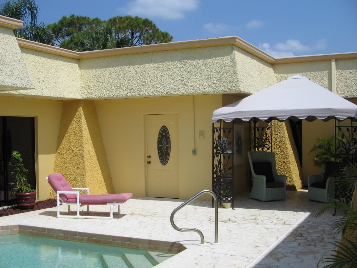A sunny patio with a pool, lounge chair, and an umbrella-covered seating area.