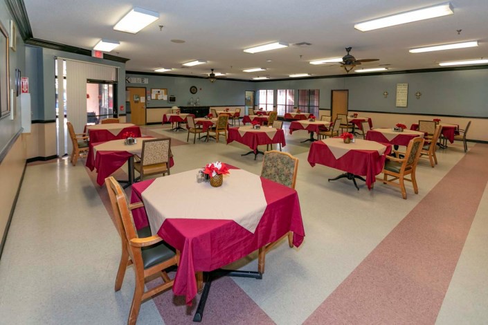 A spacious dining area with multiple tables covered in red tablecloths.