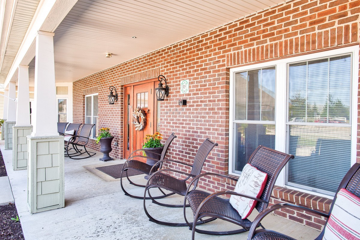 A cozy porch area featuring several rocking chairs, a brick facade, and decorative elements by the front door.