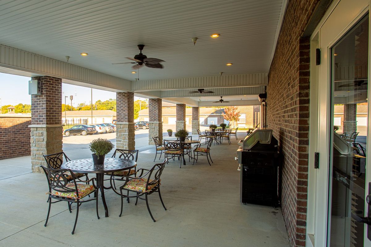 A cozy outdoor patio with tables and chairs, featuring a brick wall and ceiling fans.