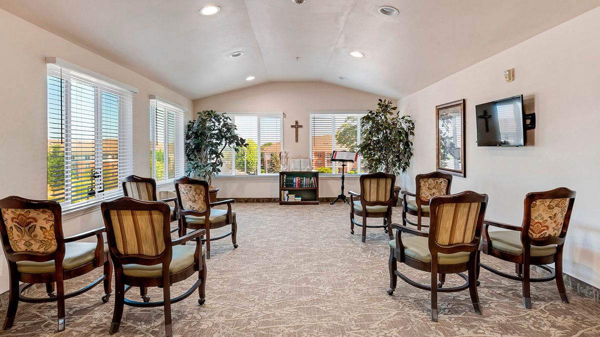 A small chapel with arranged chairs and large windows, featuring a cross on the wall.