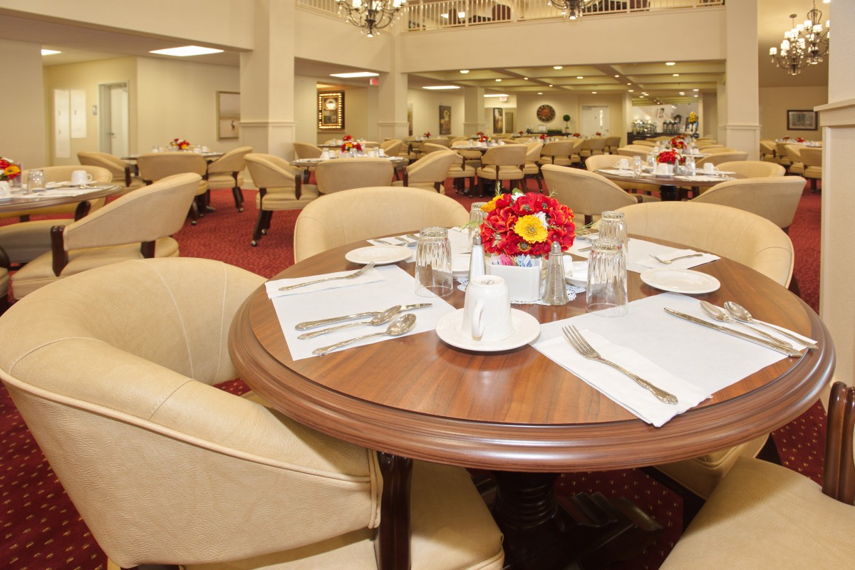 An elegantly set dining area with neatly arranged tables and chairs, adorned with floral centerpieces.