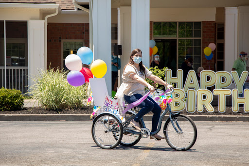 A woman joyfully rides a decorated bicycle with colorful balloons to celebrate a birthday.