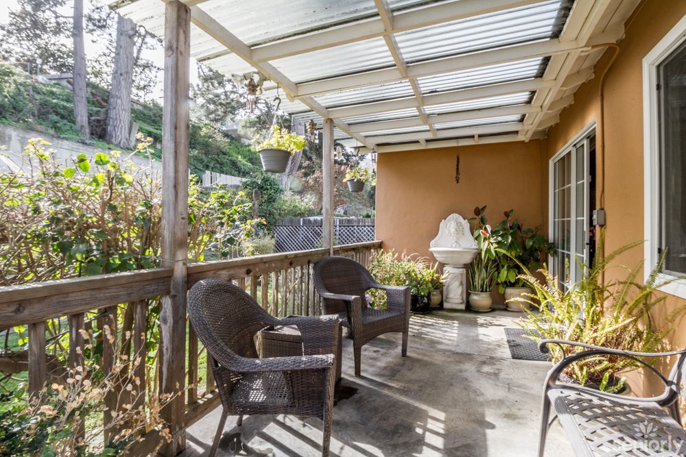 A cozy patio with wicker chairs and a fountain, surrounded by lush plants under a clear roof.