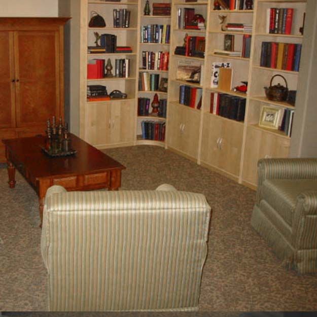 A cozy living room featuring bookshelves filled with books, a striped armchair, a wooden coffee table, and carpeted flooring.
