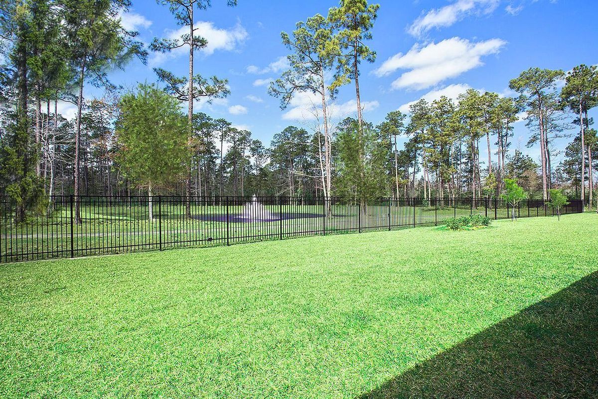 A scenic backyard with a view of a pond and surrounding trees, enclosed by a fence.