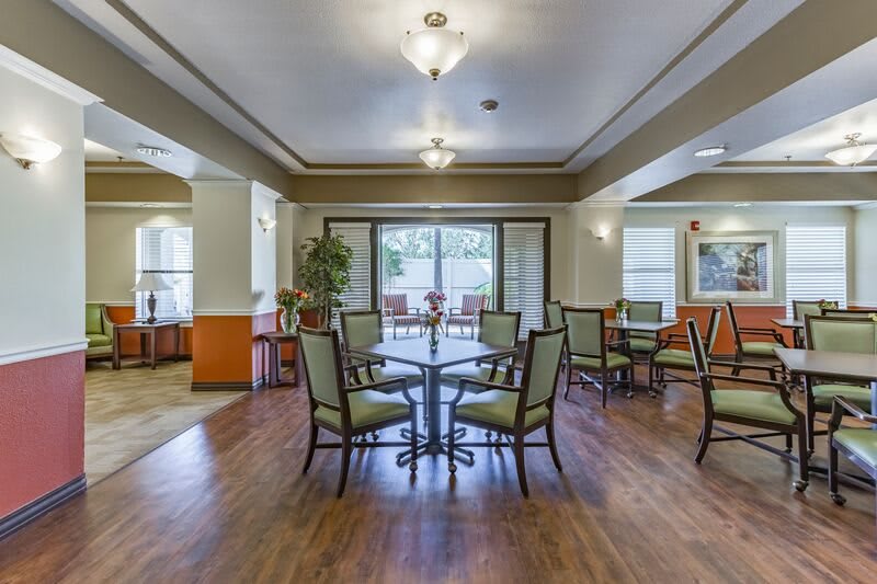 A spacious and elegantly designed dining area with wooden flooring, featuring tables and chairs under soft ceiling lights.
