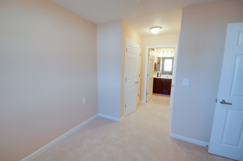 A view of a carpeted hallway leading to a bedroom with an attached bathroom.