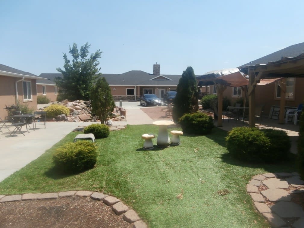 A well-maintained garden with a lawn, bushes, and a patio in front of a house on a sunny day.