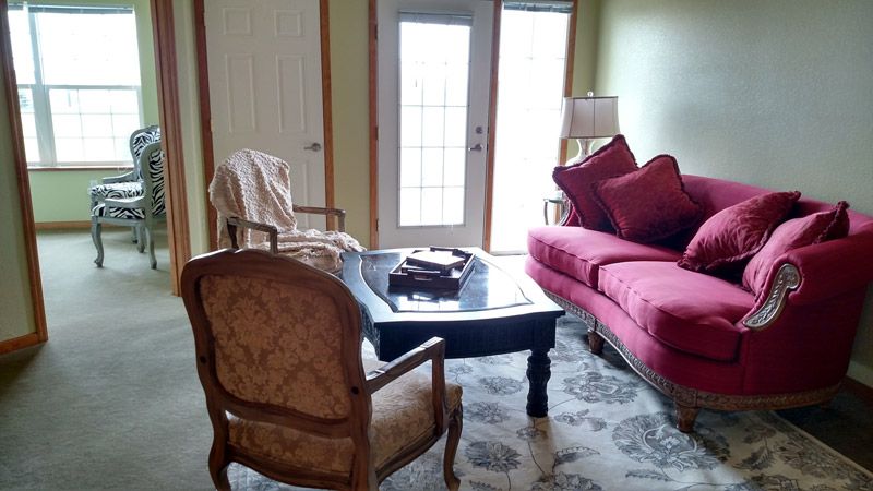A cozy living room featuring a red sofa, two chairs, a coffee table, and a carpet with natural light streaming through the glass doors.