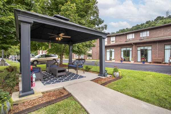 A modern gazebo with comfortable seating is set in a green lawn, adjacent to a contemporary building.