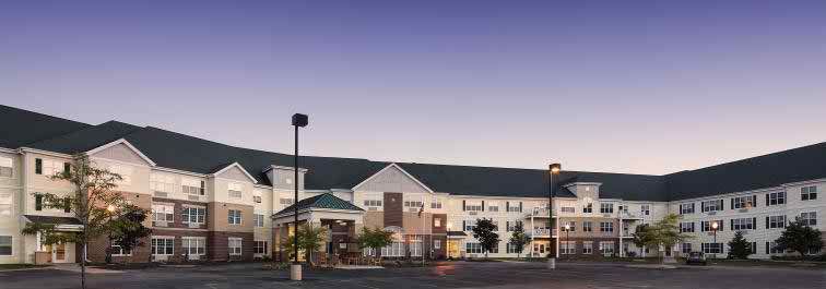 This image shows the exterior of a hotel building at dusk, with lights illuminating the entryway and a parking lot in the foreground.