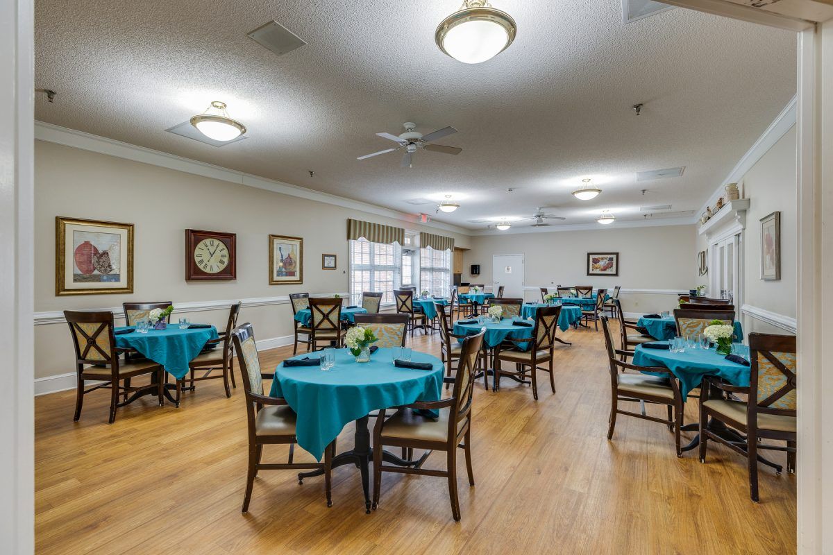 A neatly arranged dining room with tables and chairs covered in teal tablecloths.