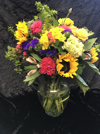 A vibrant bouquet of various flowers, including sunflowers and colorful blooms, displayed in a glass vase.