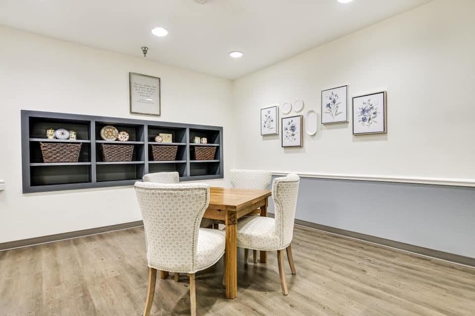 A cozy, modern room with a wooden table and upholstered chairs, adorned with decorative shelving and framed artwork.
