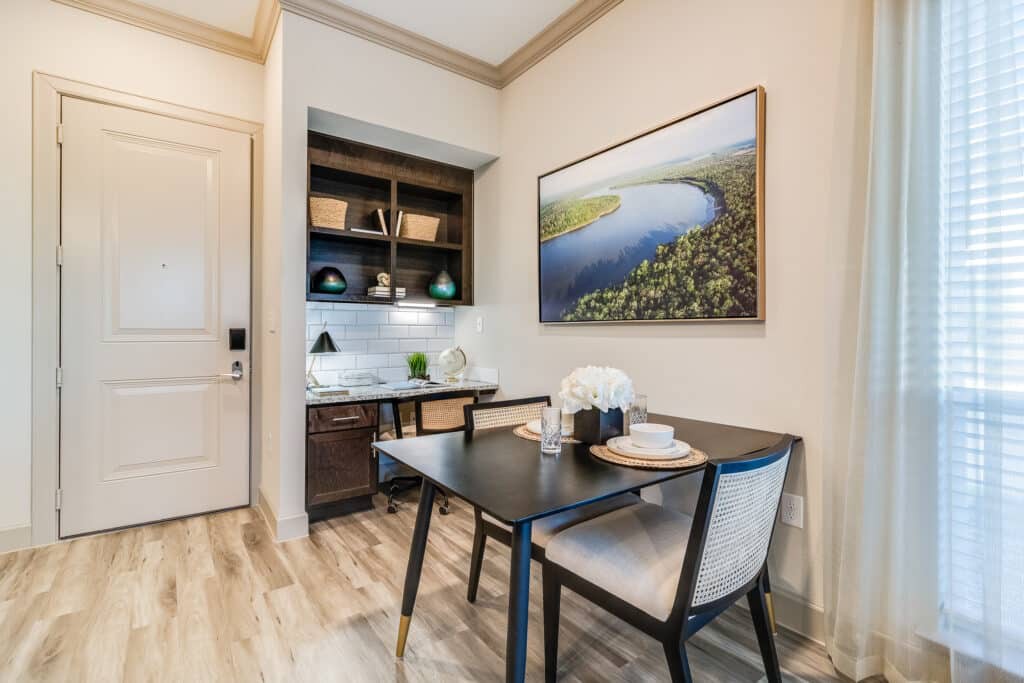 A modern dining area with minimalist decor, featuring a table set for two and a scenic artwork on the wall.