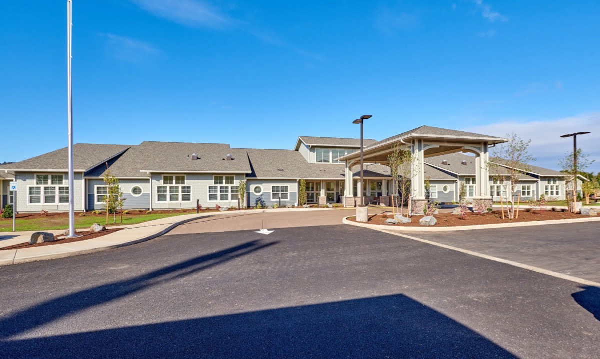 A modern residential building with a driveway and main entrance under a clear blue sky.