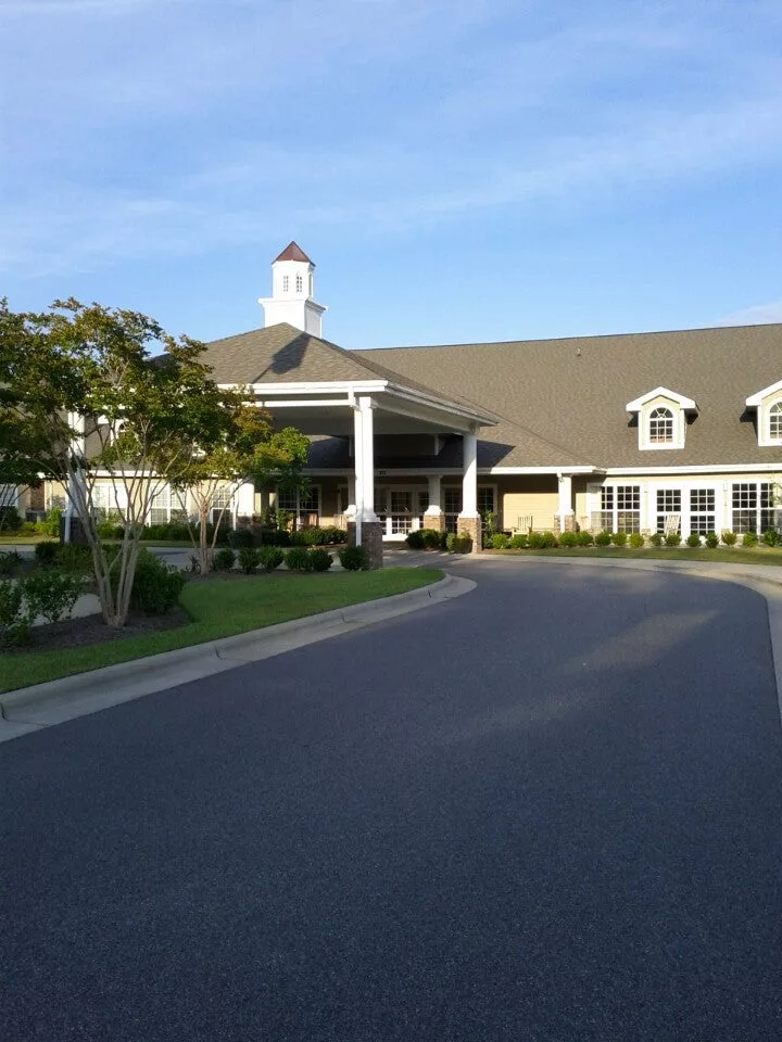 A large building with a driveway and landscaped gardens under a clear blue sky.