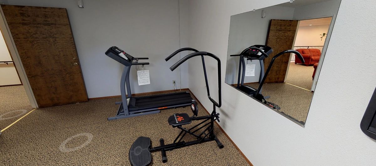 A small gym room with a treadmill and exercise equipment next to a mirror.