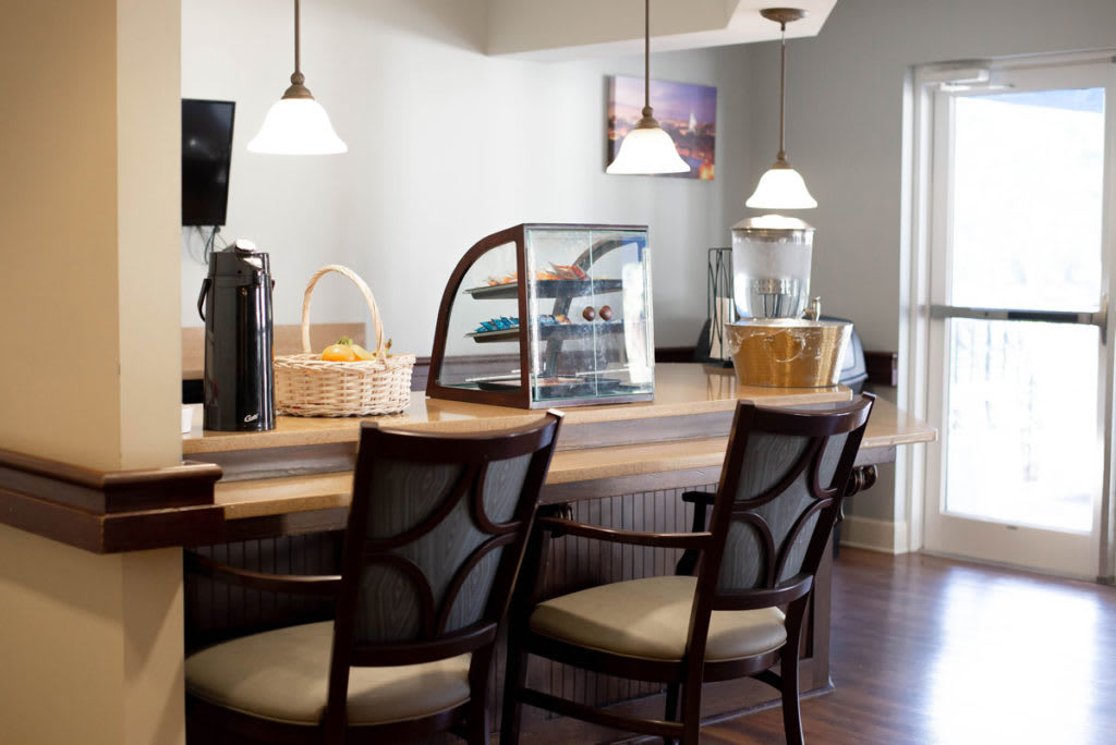 A cozy cafe interior with chairs around a wooden counter, featuring pastries and warm lighting.