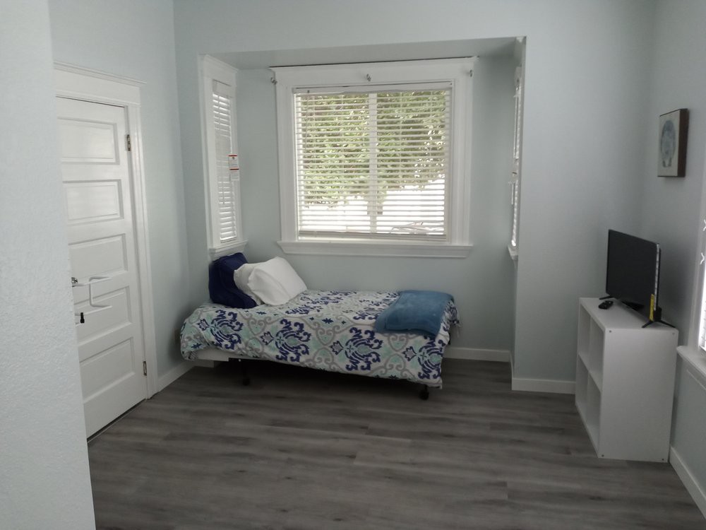 A minimalist bedroom with a single bed, light blue walls, and a large window.