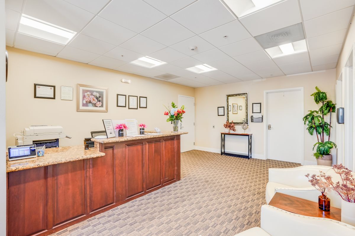 A neat and welcoming office reception area with a wooden desk, floral decorations, and framed art on the walls.