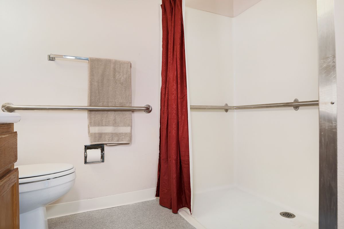 An accessible bathroom with a red shower curtain and grab bars.