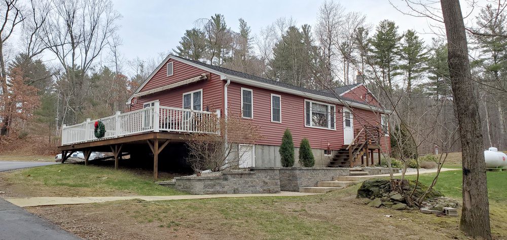 A red house with a porch and deck, surrounded by trees in a rural setting.