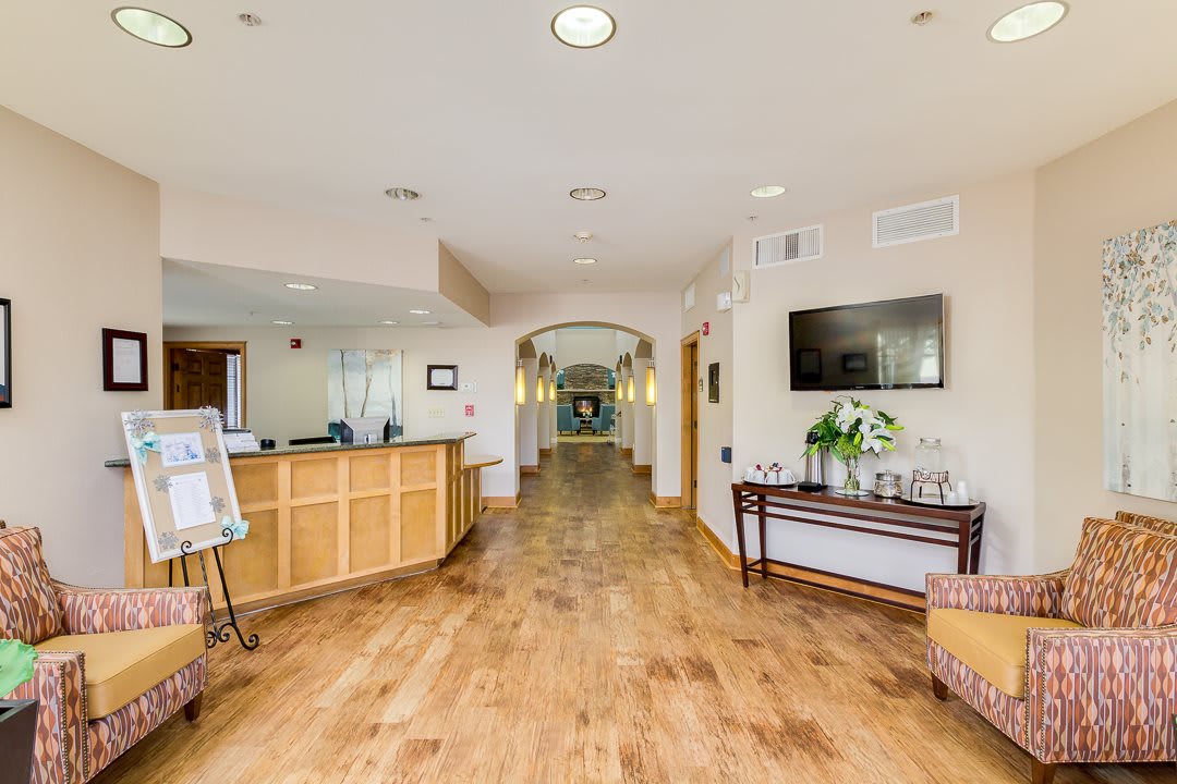 A modern lobby with a reception desk and wooden flooring leading to a hallway.