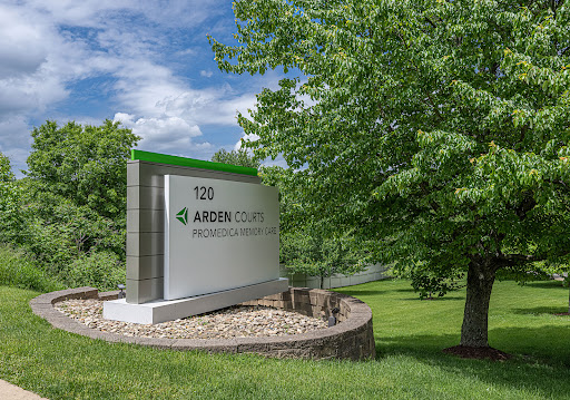 A sign for a business surrounded by lush greenery and a partly cloudy sky.
