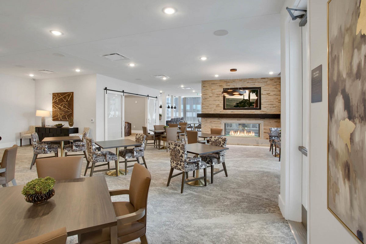 A modern seating area with tables and chairs, featuring a fireplace and ample lighting.