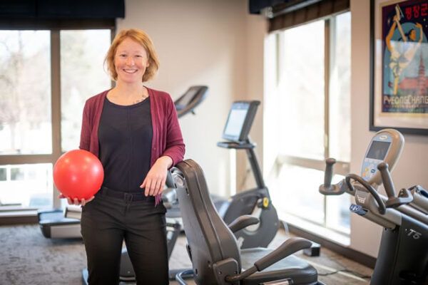 A person standing in a gym holding a red exercise ball.