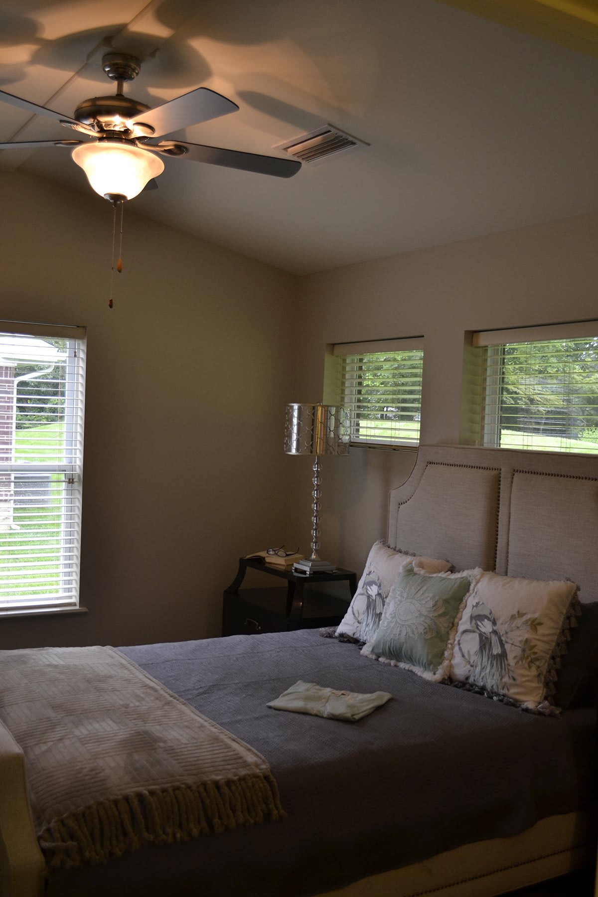A cozy bedroom with a large bed, windows, and a ceiling fan.