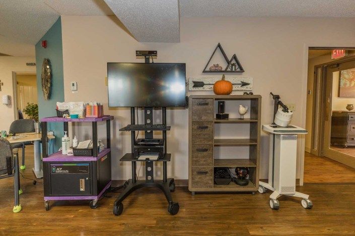 A neatly organized office space featuring a TV stand, storage shelves, and a cart.