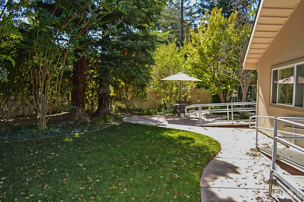 A serene garden setting with a pathway leading to an outdoor patio area under trees.