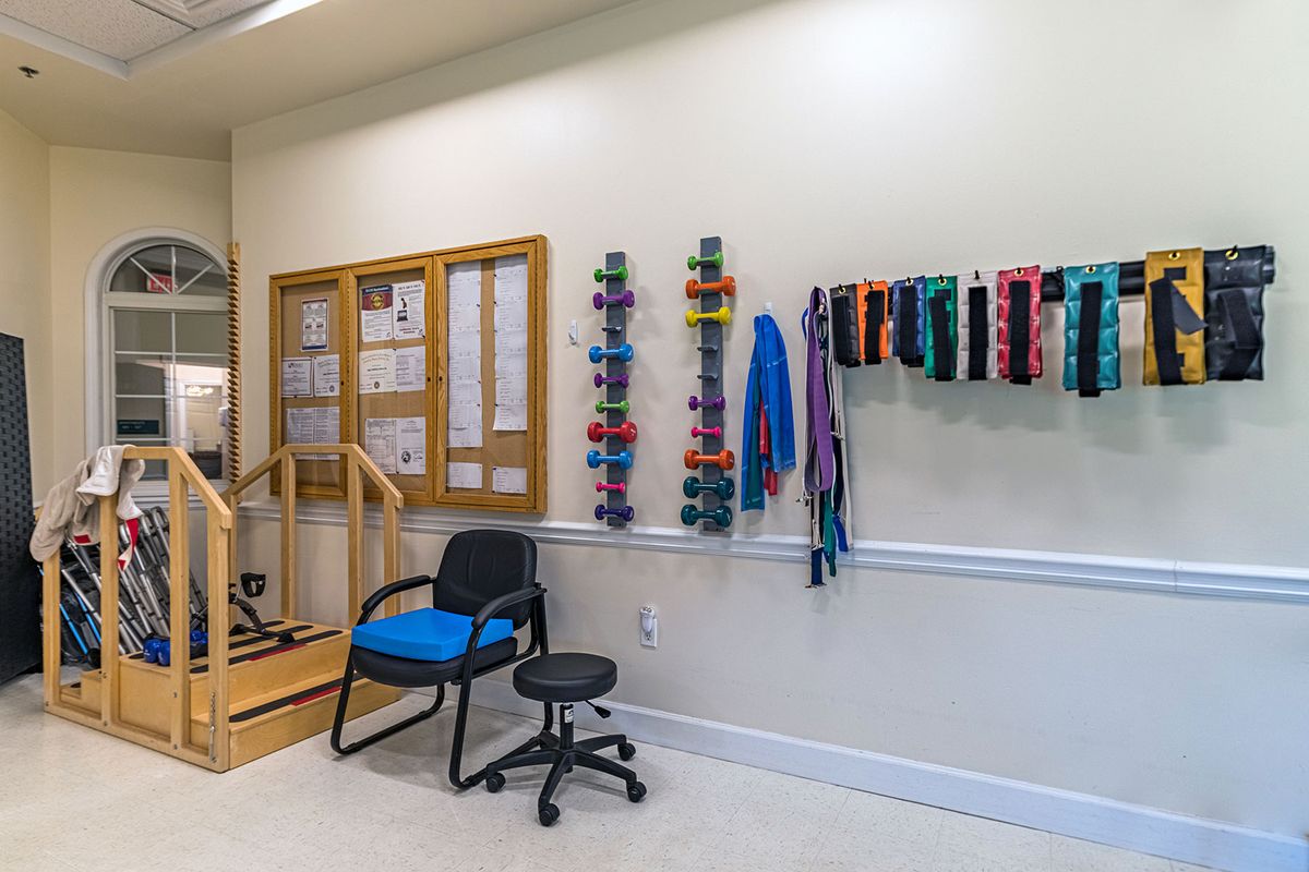 A rehabilitation room featuring exercise equipment, therapy bands, chairs, and rehab stairs.