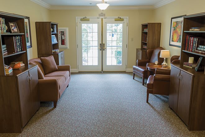 A cozy living room with sofas, chairs, and bookshelves facing glass doors.