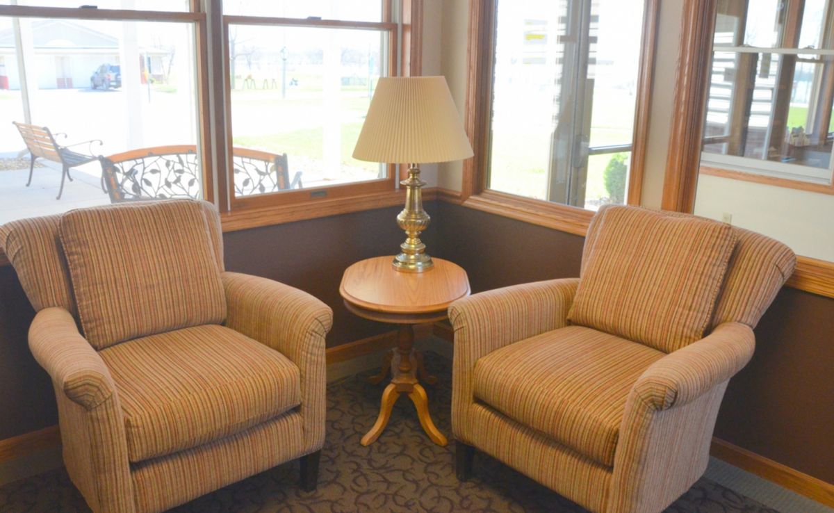 A cozy seating area with two armchairs, a small round table, and a lamp by the window.