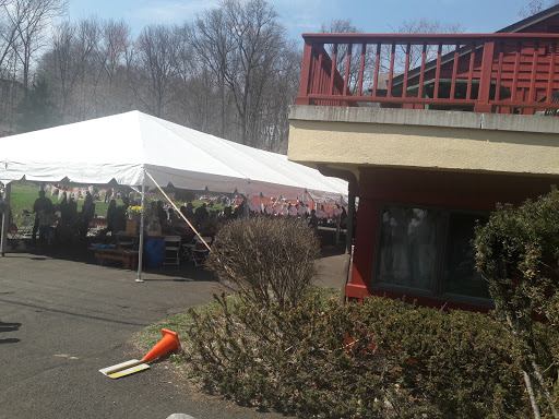 A spacious outdoor tent set up next to a building, surrounded by greenery on a sunny day.