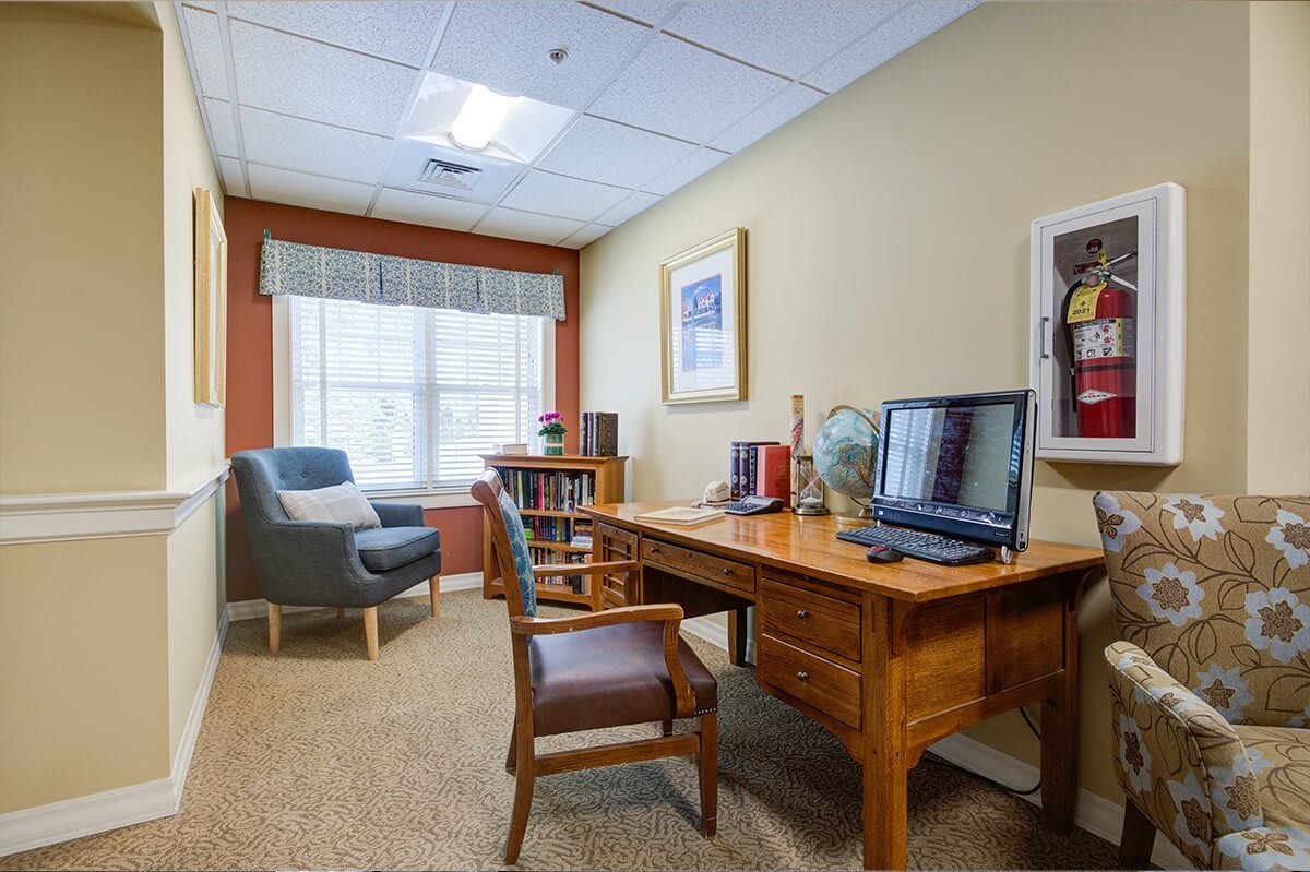 A neatly organized office space with a desk, computer, and bookshelf by the window.