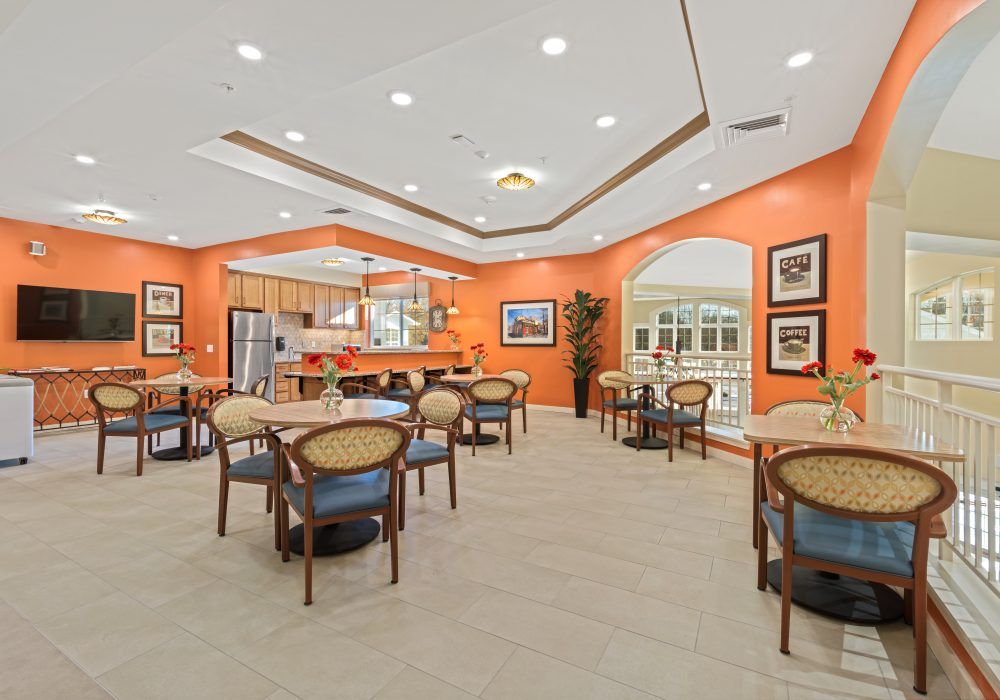 A modern dining area with orange walls, featuring tables and chairs adjacent to a kitchen.