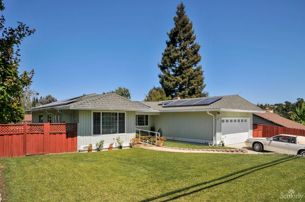 A suburban house with solar panels on the roof, surrounded by a neatly maintained lawn and a large tree.