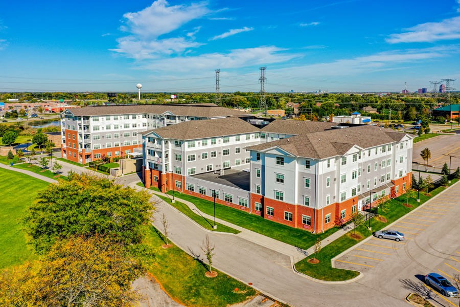 Aerial view of a residential apartment complex with surrounding greenery and a parking area.
