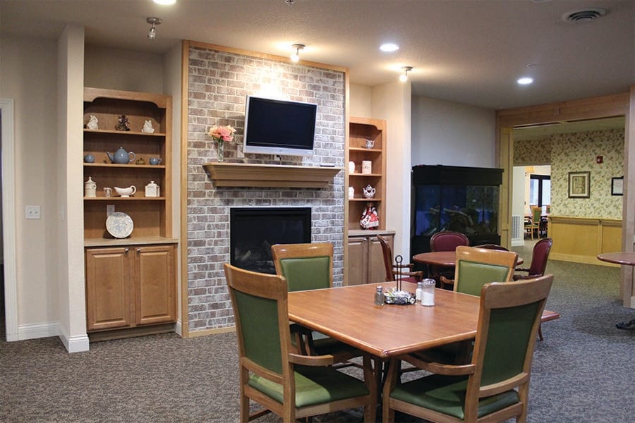 A cozy living room and dining area featuring a fireplace, television, and wooden furnishings with decorative shelves.