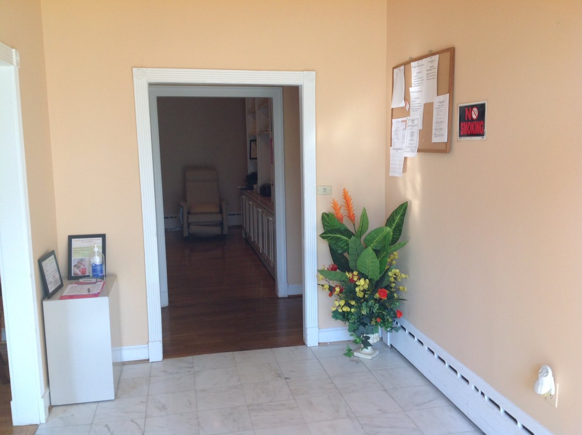 A hallway with a doorway, decorated with a potted plant and a notice board on the wall.